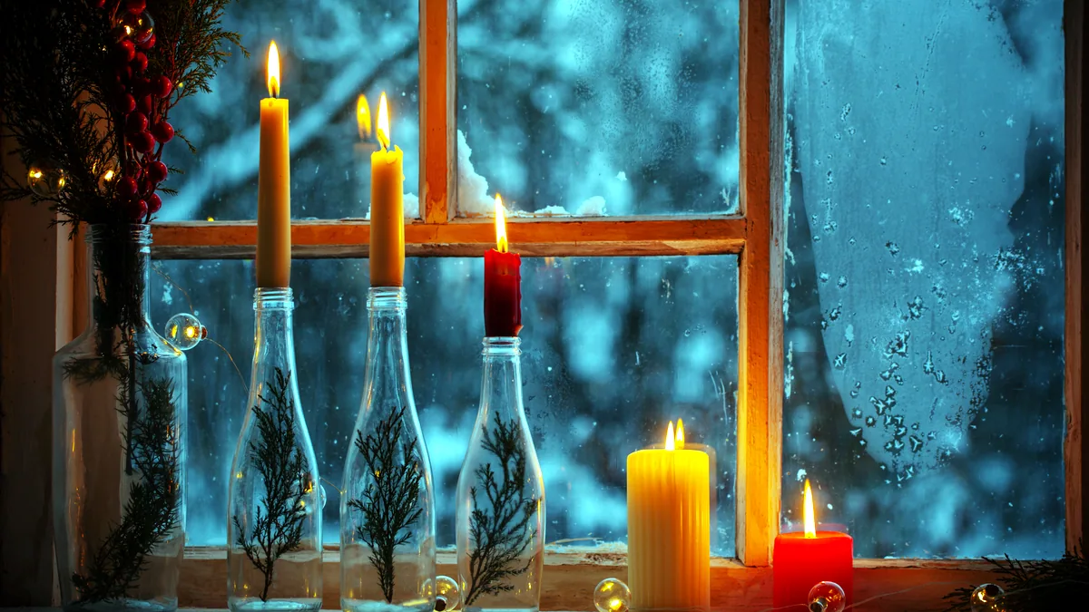 Frost patterns on a window with warm candlelight glowing inside.