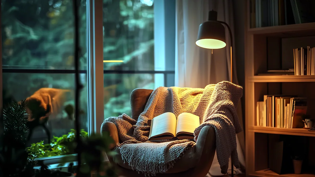 A worn armchair beside a table lamp glowing in a quiet room.