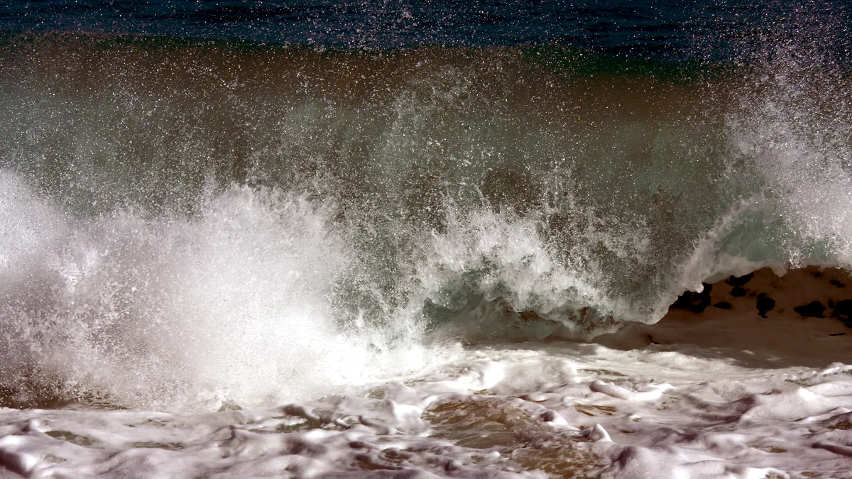 Waves rolling onto a sandy shore beneath a wide blue sky.