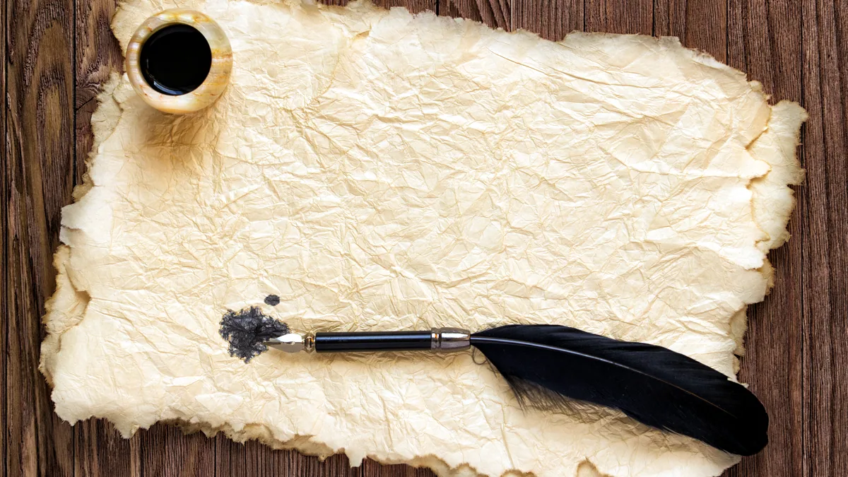 A quill pen resting beside an inkwell on old parchment.